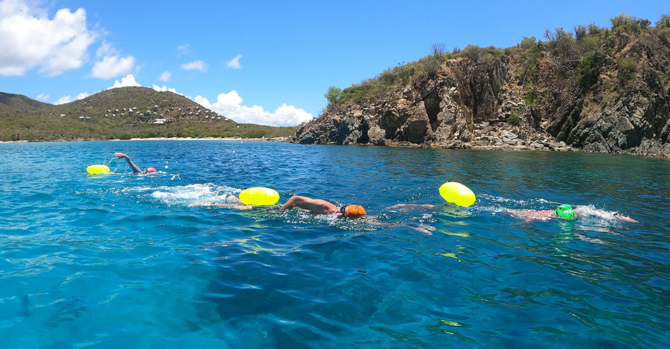 Three people swimming in the ocean near an island